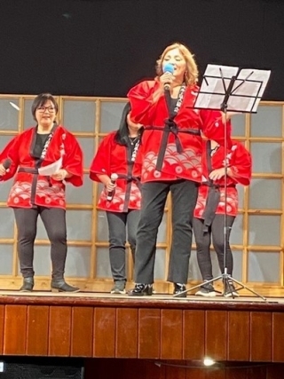 Participantes en el escenario, vestidos todos con trajes típicos japoneses “happi”, cantando una canción con tres acompañantes 