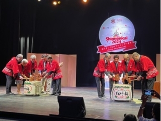 Los invitados con hapi rojo, vestimenta tradicional japonesa, están a punto de abrir 2 barriles de sake en el escenario