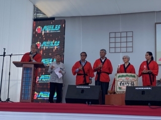 Embajador YAMAMOTO con hapi rojo, vestimenta tradicional japonesa, dirige sus palabras del brindis en el escenario