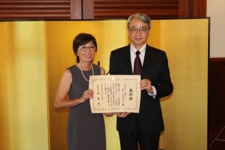 La Sra. Galla posa mostrando su diploma con el Embajador Yamamoto