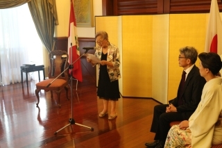 Embajador YAMAMOTO y su esposa sentados, escuchando las palabras de la consejera IGARASHI que se encuentra de pie
