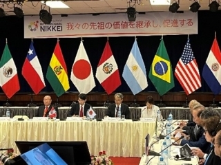 El Presidente de APJ Sr. Okada, el Embajador YAMADA, el Embajador YAMAMOTO, La Prosecretaria de APJ Sra. Hiraoka se encuentran sentados con las banderas en frente.