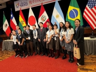 El Embajador YAMADA en la toma de foto conmemorativa con los participantes frente a las banderas.
