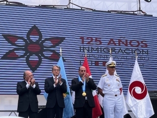 En la pantalla figura “125 años de la Inmigración Peruana Japonesa” y los 4 representantes se encuentran delante de la pantalla.
