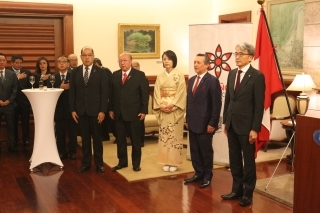 Embajador YAMAMOTO, su esposa y los asistentes, ubicados delante del banner con el logo del 125 aniversario de la inmigración japonesa al Perú, cantan los himnos nacionales del Perú y Japón