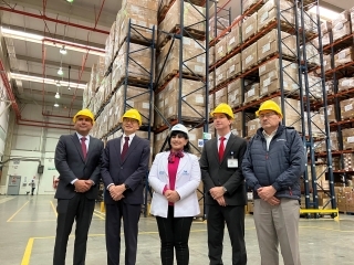 El Embajador YAMAMOTO posa para una foto junto con la Presidenta Maria Elena Aguilar de EsSalud y el Gerente General Rogerio Marcondes de Salog en frente de gigantescas estanterías de farmacéuticos