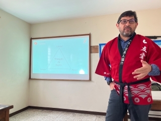El instructor con happi, bata tradicional japonesa, explicando con material de PowerPoint proyectado en el fondo
