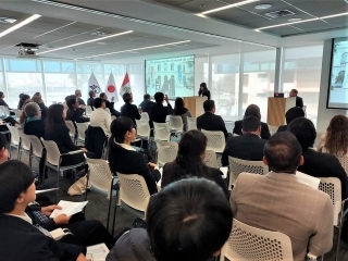Una voluntaria de JICA presentando su informe y los demás asistentes prestan atención a su exposición