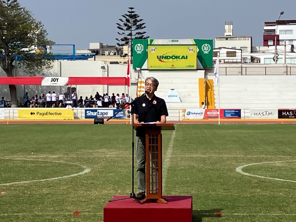 El Embajador YAMAMOTO dirige las palabras del saludo en la ceremonia protocolar en el podio colocado en la pista de atletismo