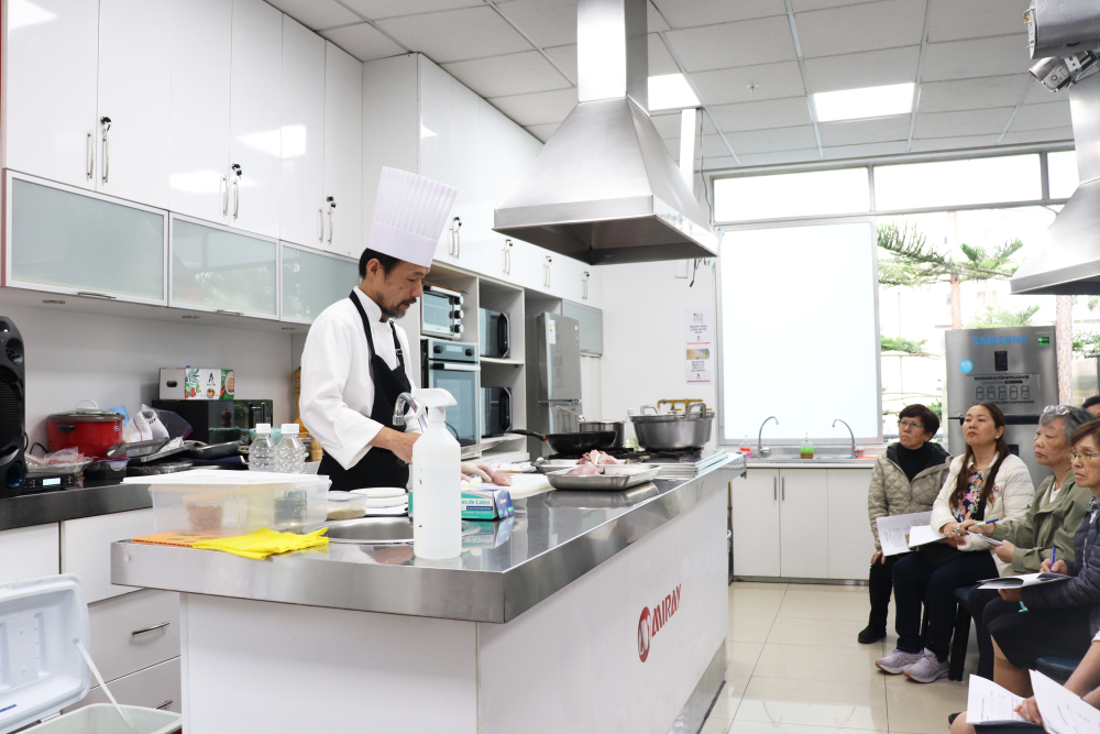 El Sr. Satoshi Yamamoto, chef de la residencia del embajador de Japón, está dictando la clase de cocina japonesa ante aproximadamente 30 asistentes.