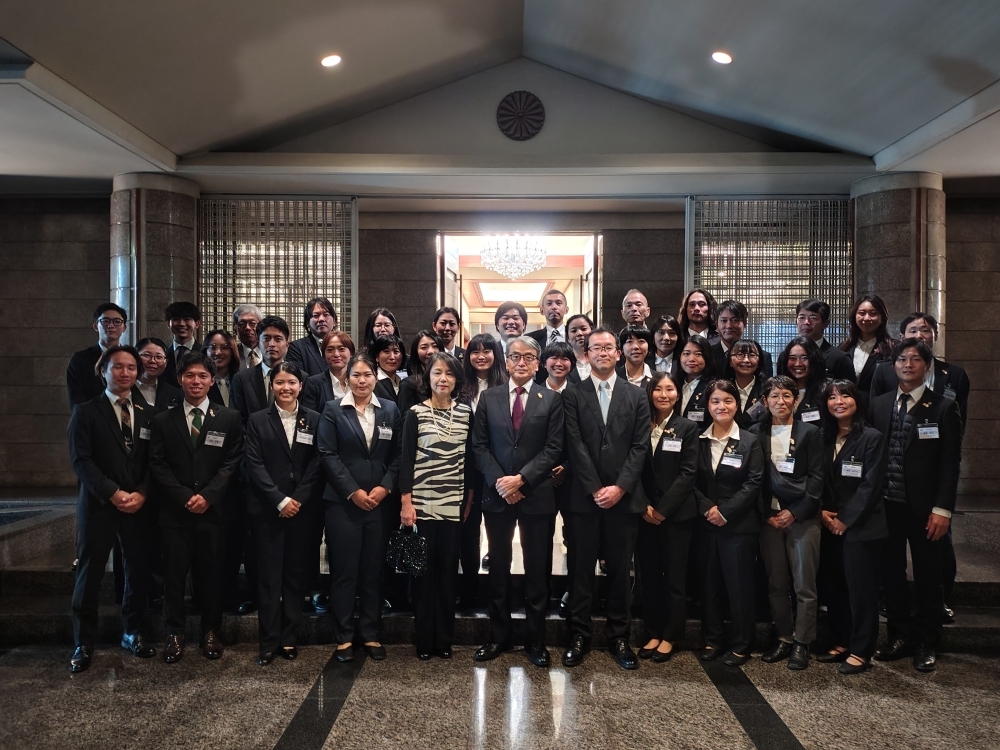 El Embajador YAMAMOTO y su esposa con los voluntarios de JICA tomándose una foto grupal frente a la entrada de la residencia