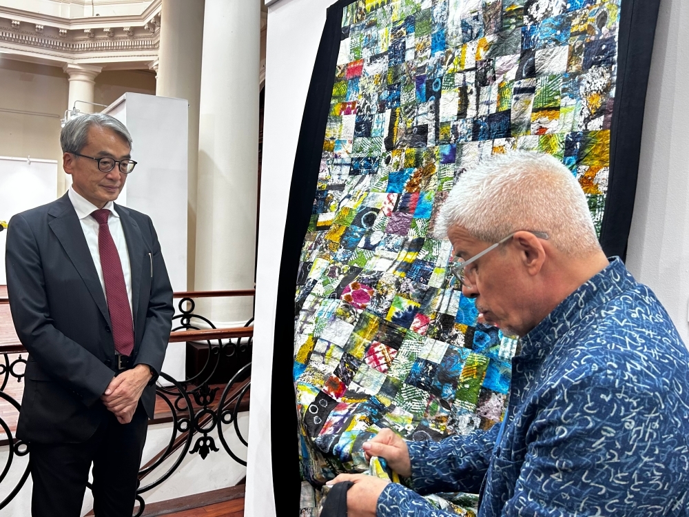 El artista Herberth Bolaños muestra una obra muy colorida al Embajador YAMAMOTO