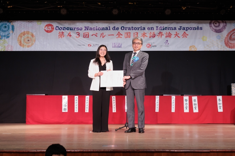 Foto del embajador YANMAMOTO con la ganadora absoluta del certamen, sosteniendo el diploma.