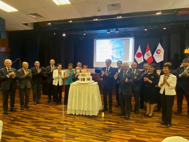 Los participantes se reúnen para la foto alrededor del pastel en celebración del centenario del natalicio del padre Manuel Kato.