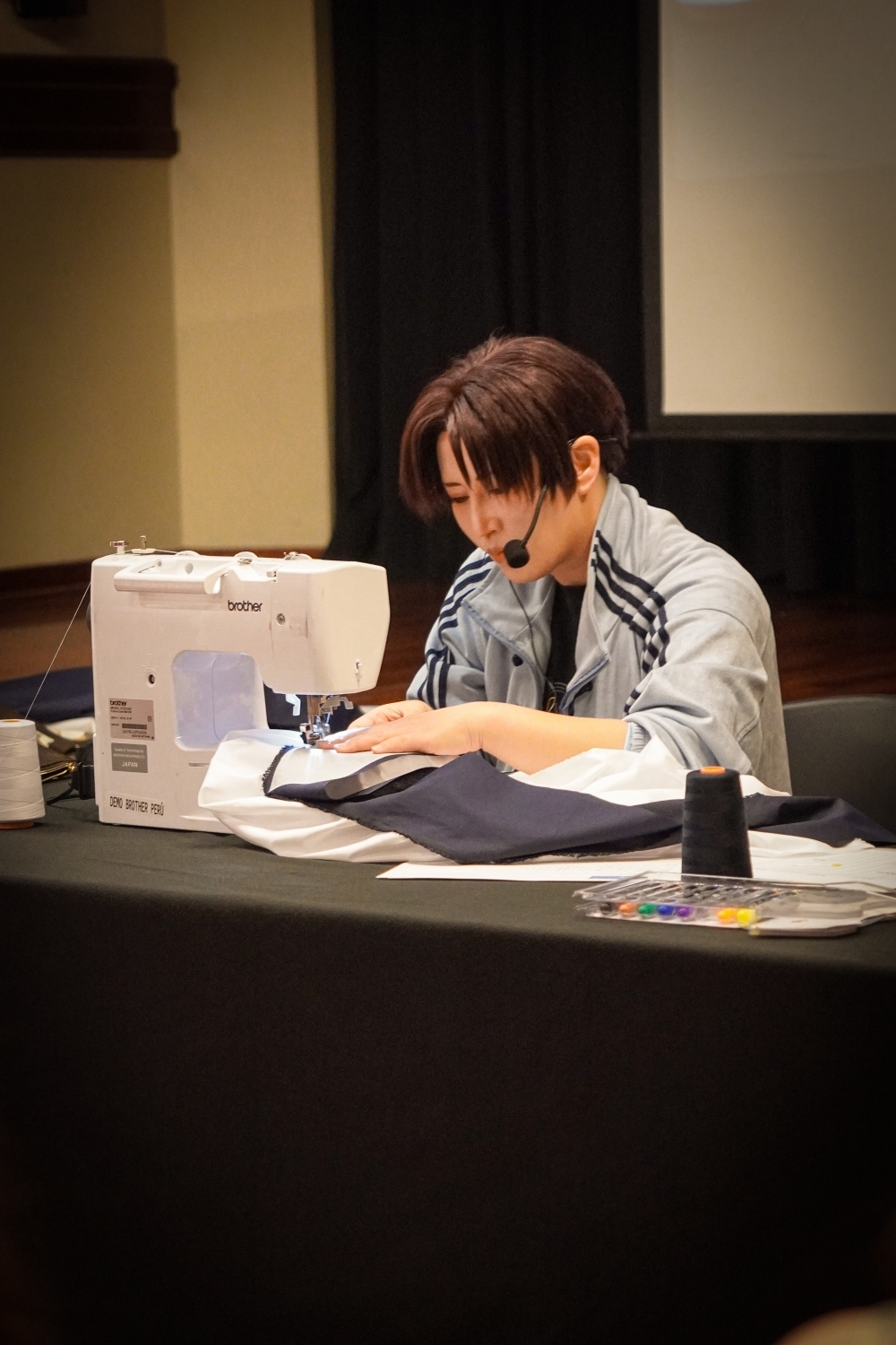 La cosplayer ARIKAWA　Reika al lado izquierdo mostrando cómo se confecciona un haori, utilizando una tela y una máquina de coser.