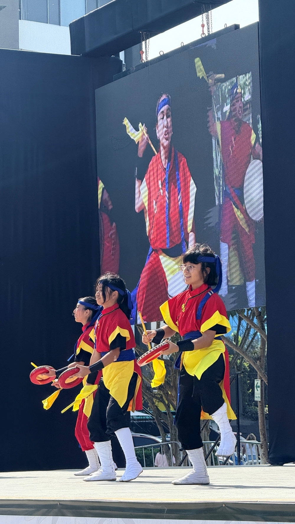 Tres integrantes de la agrupación Bunayaga presentándose en el escenario con un número de tambores taiko y danza